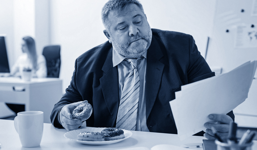 overweight businessman at desk eating donuts